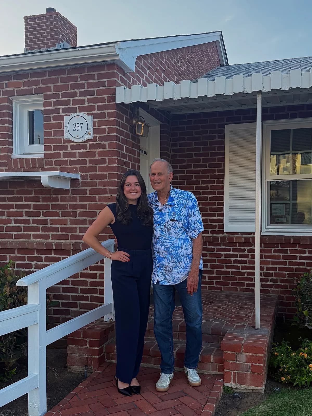 Young woman and older man smiling on the brick porch of a house numbered 257.